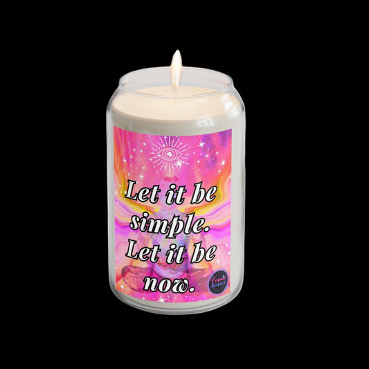 Candle with a colorful label on a white surface with a plant and watch in the background